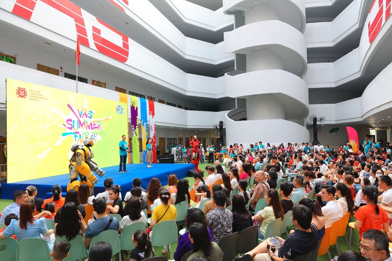 A group of people in a room with a stage and a person in a yellow suitDescription automatically generated